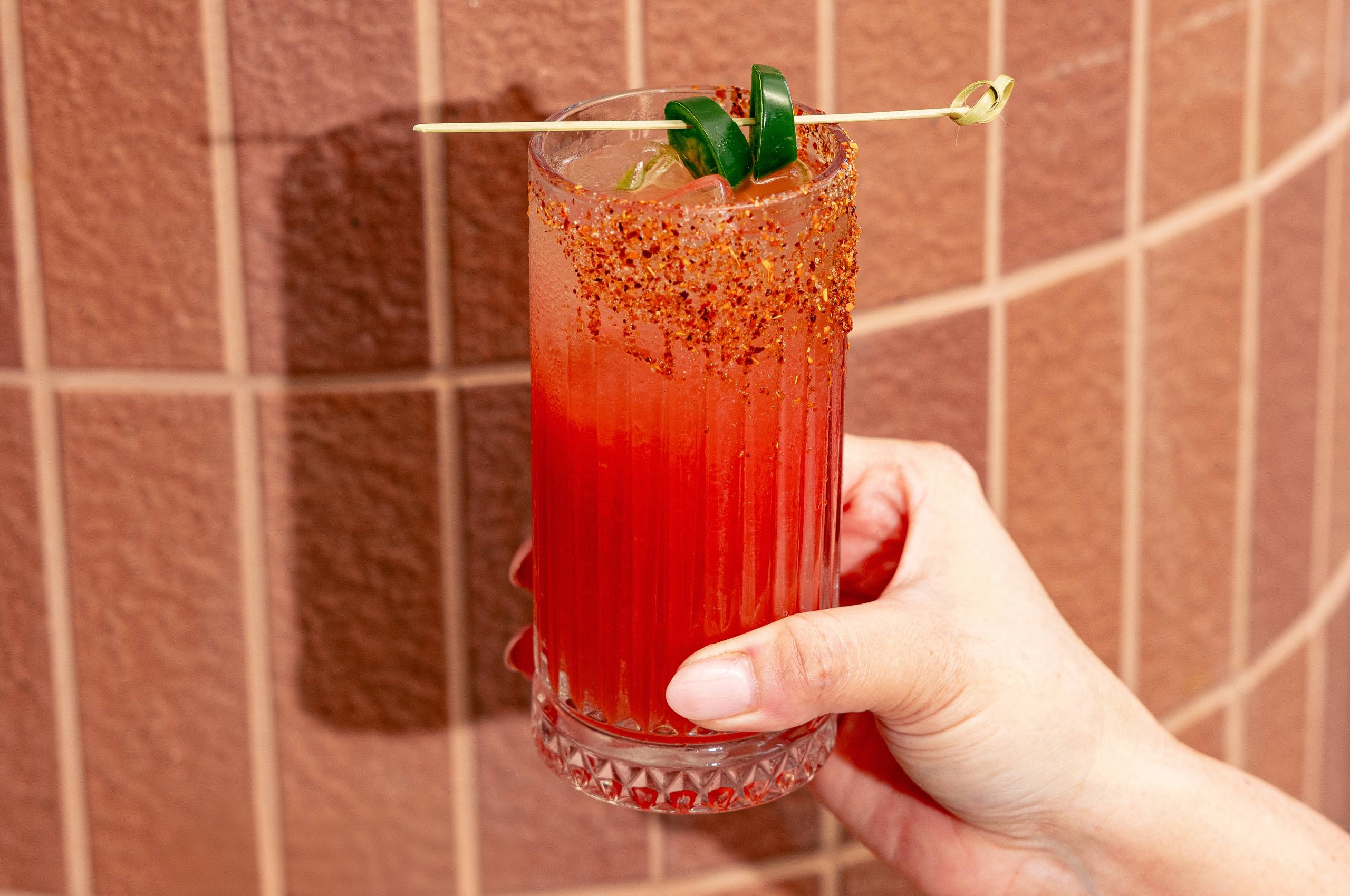 Image of a hand holding a Tromba Tequila Sandia Paloma against an aesthetic pink tile wall.
